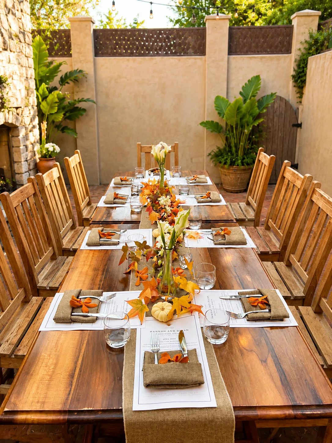 Long outdoor dinner table set for a celebration with a fall leaf and floral centerpiece runner