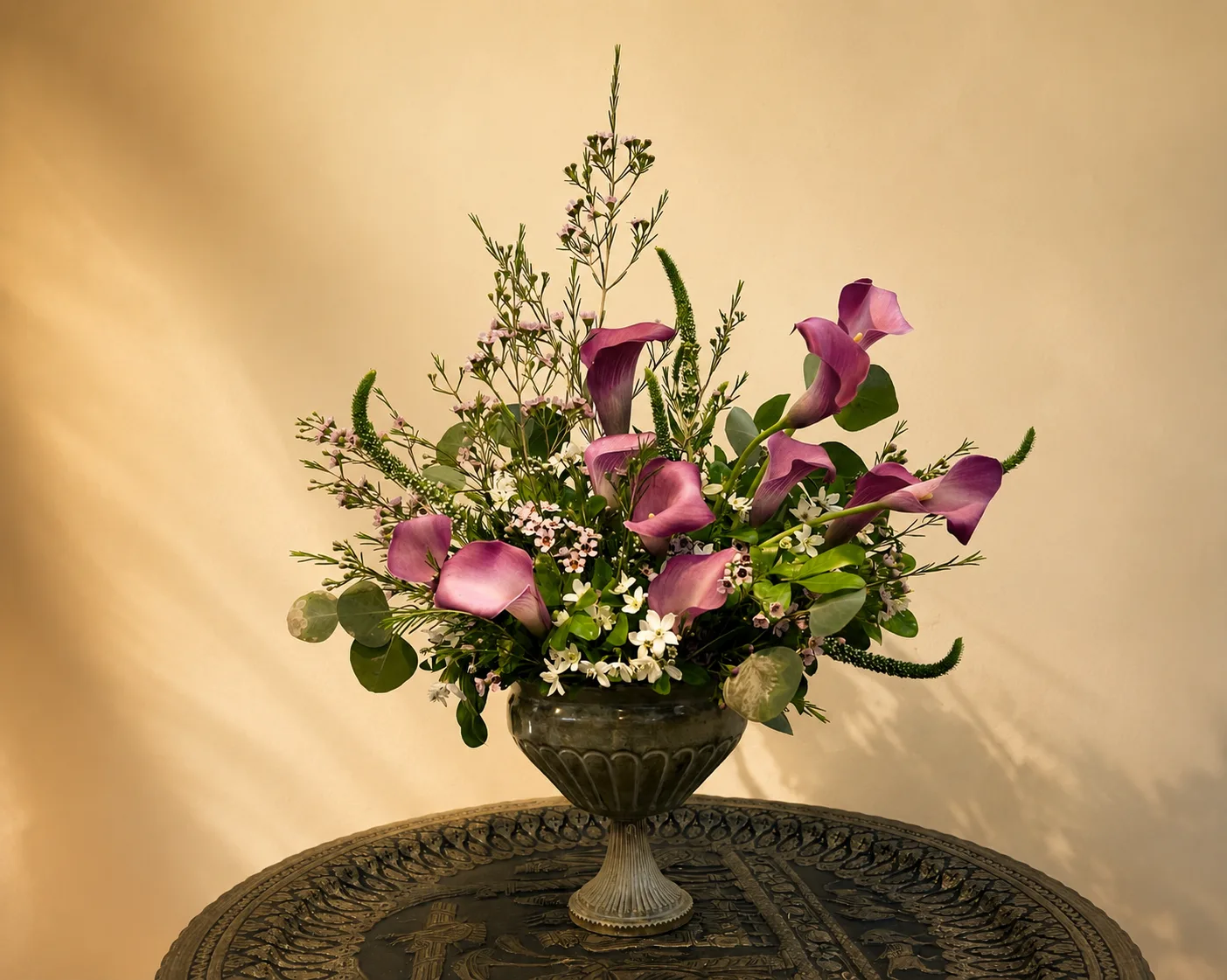Mauve calla lily and wax flower arrangement in a carved stone urn