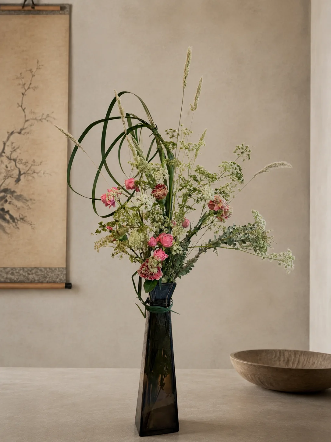 Pink carnation and Queen Anne's lace arrangement in a tall dark glass vase against a Japanese ink scroll