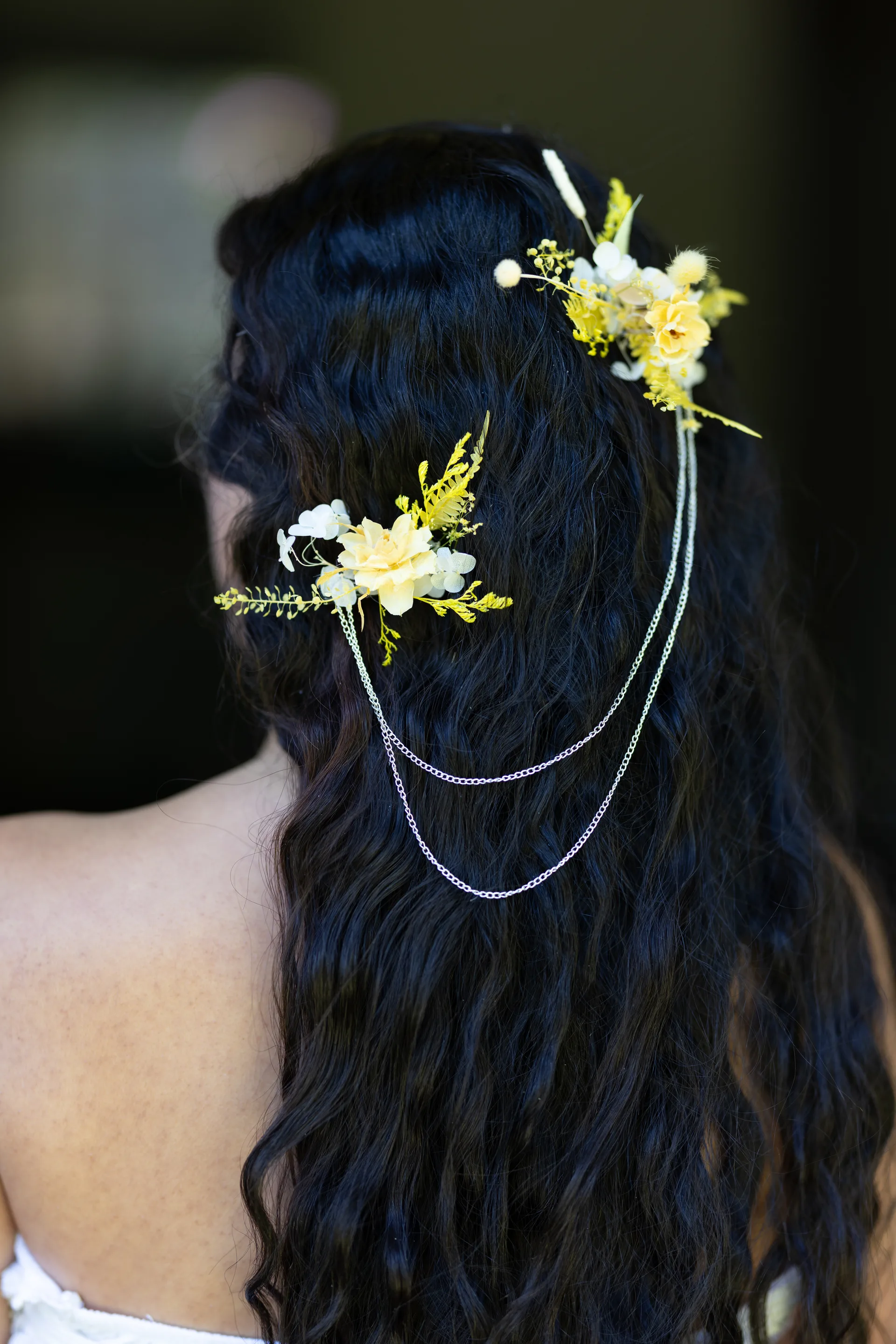 Back view of yellow dried flower hairpieces linked by delicate chains through long dark hair