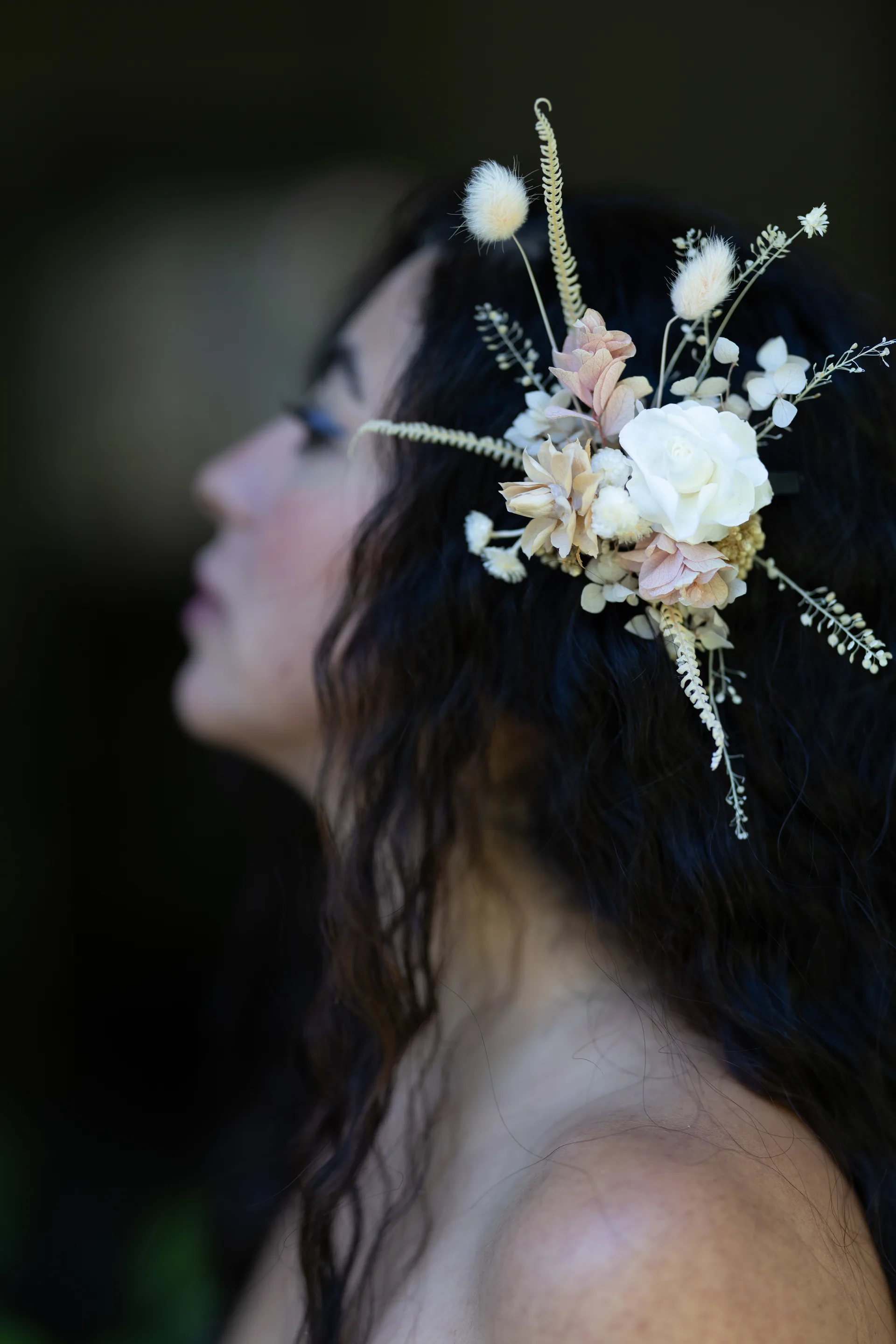 Side profile of a dried flower and dried grass hairpiece in cream and blush tones nestled in dark hair