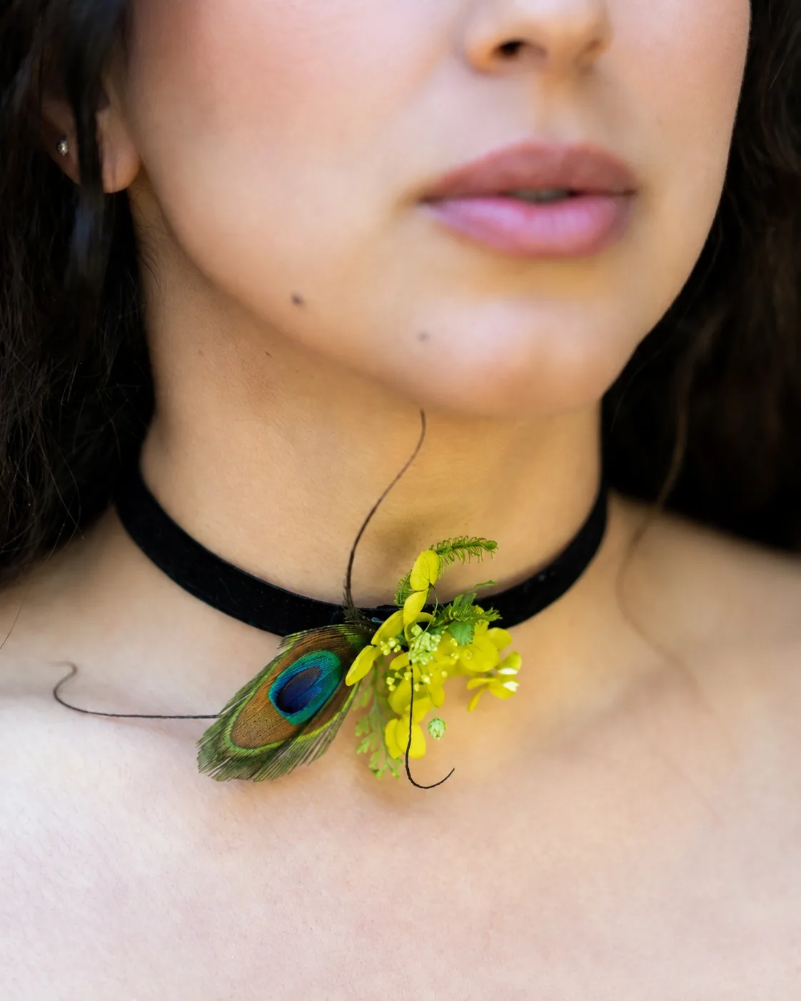 Close-up of a black choker with a peacock feather and yellow dried flower cluster at the throat