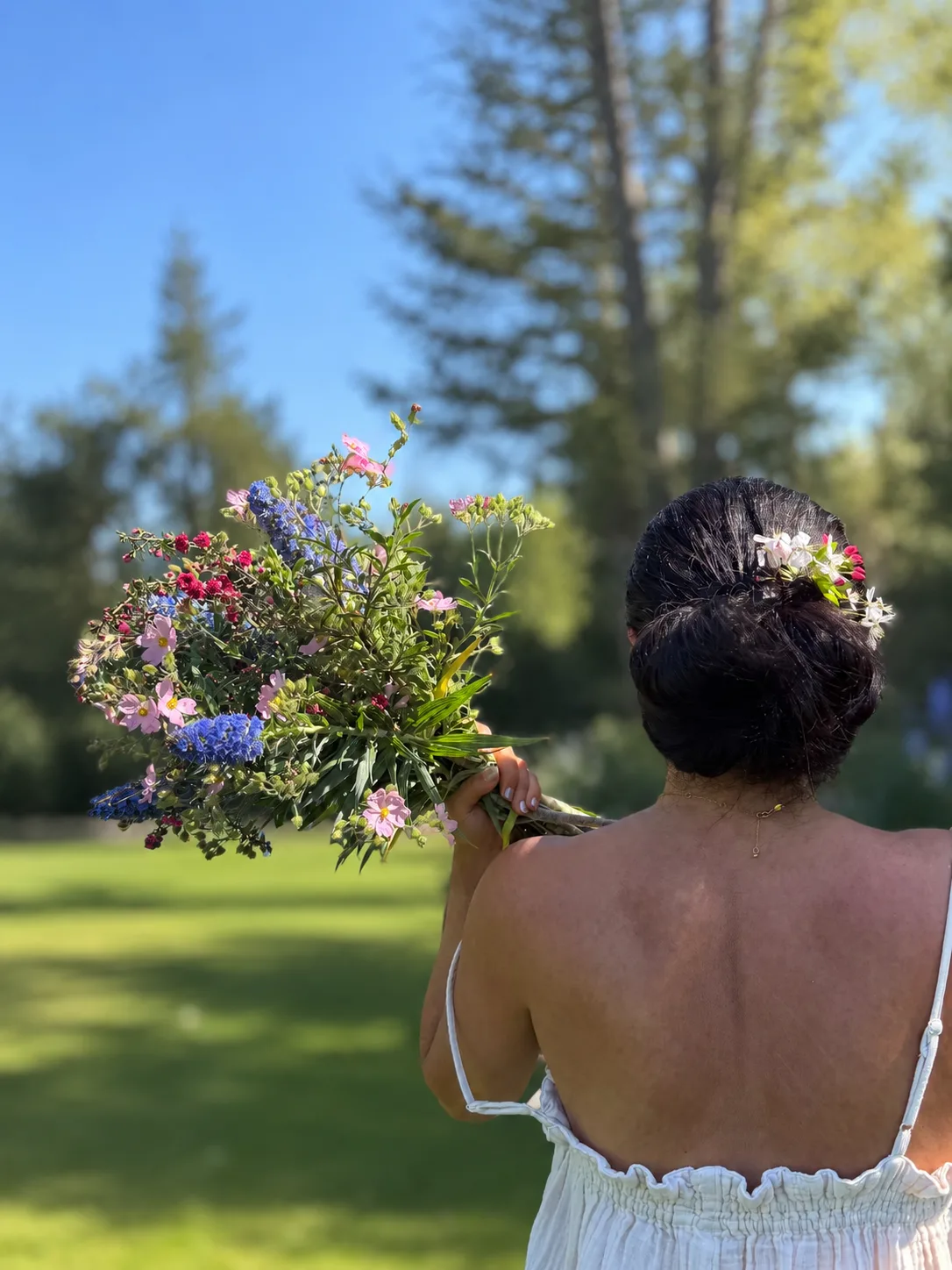 Woman holding a wildflower bouquet aloft against a blue sky, flowers woven into her updo