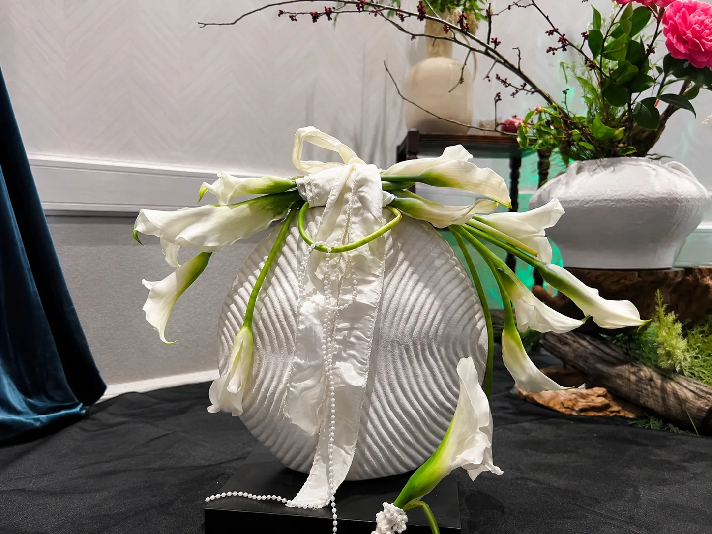 White calla lily bouquet tied with pearl strands and ribbon, draped over a ribbed white vase