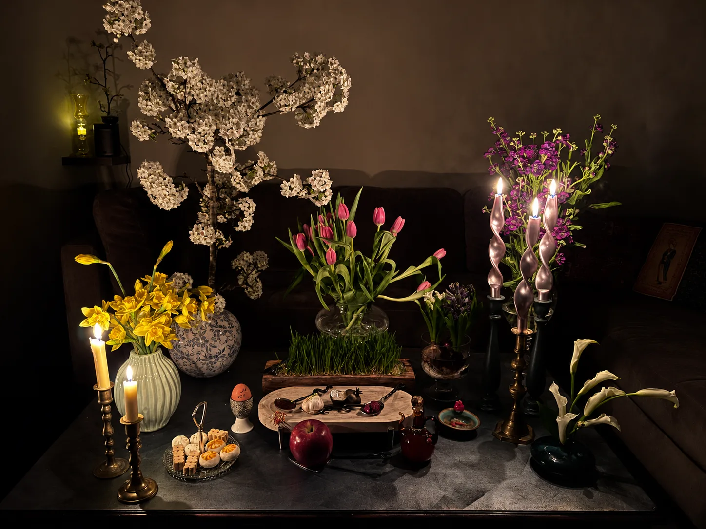 Persian ceremonial table spread with tulip, daffodil, and hyacinth arrangements, lit candles, and traditional Nowruz items