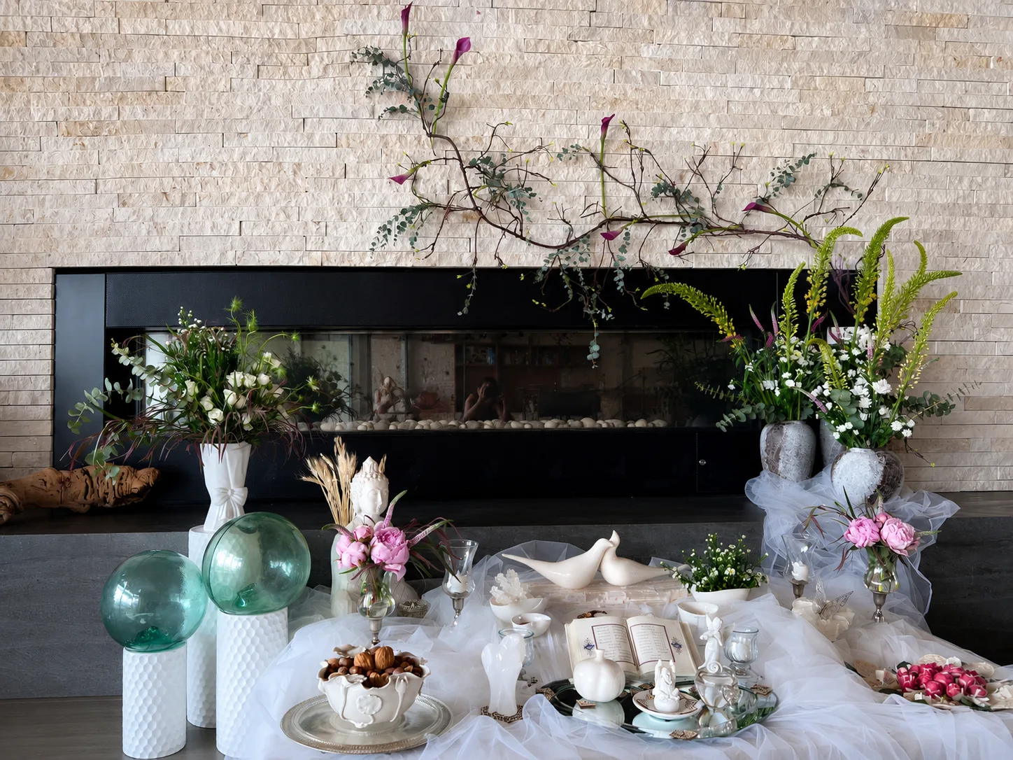 Branch and calla lily floral installation mounted above a stone fireplace, flanked by tall floral arrangements at a Persian sofreh aghd ceremony